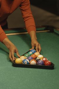 A close-up view of a person arranging billiard balls in a triangle on a pool table for a game.