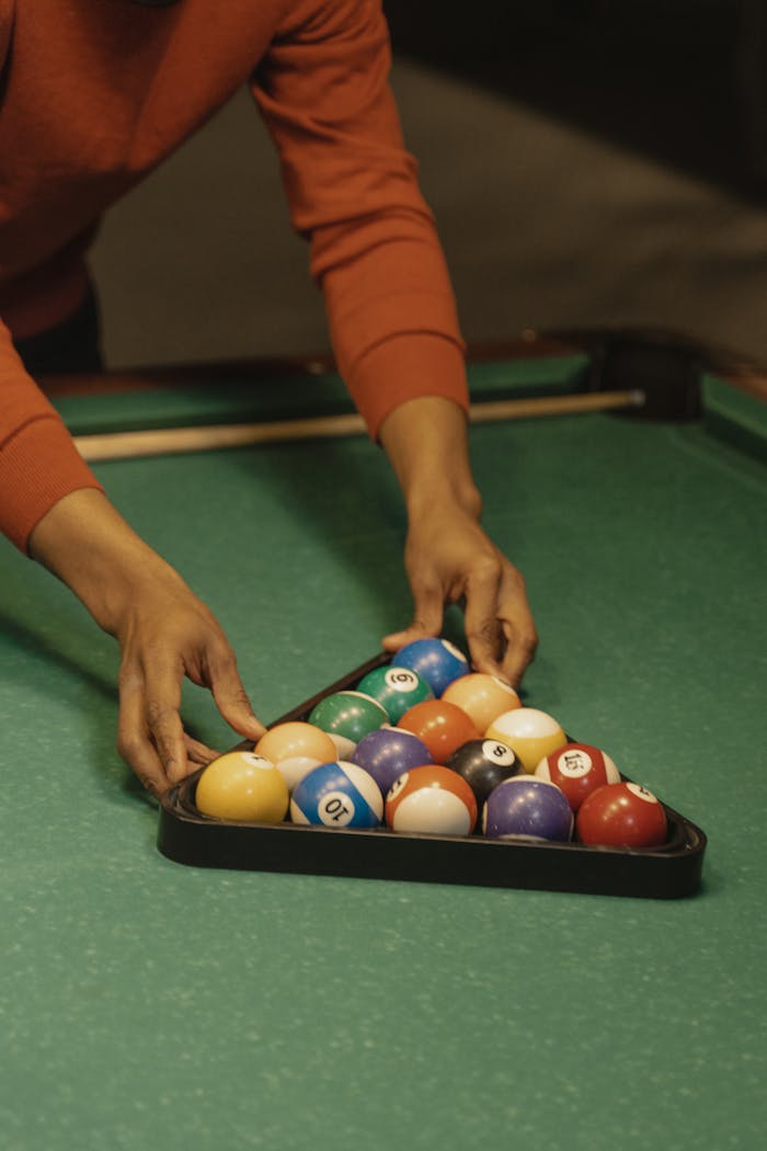 A close-up view of a person arranging billiard balls in a triangle on a pool table for a game.