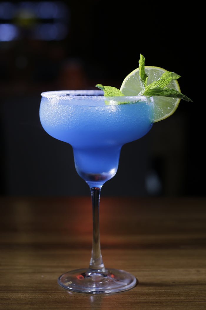 A vibrant blue margarita cocktail with lime and mint garnish on a wooden table.