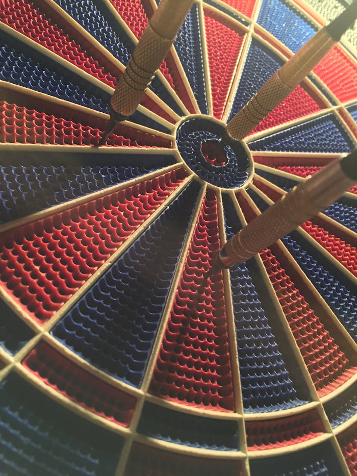 round-black-and-red-dart-board-416816 A detailed view of a dartboard with darts in the bullseye, showcasing a competitive sports moment.